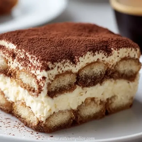 layered tiramisu slice with cocoa powder on a white plate beside espresso