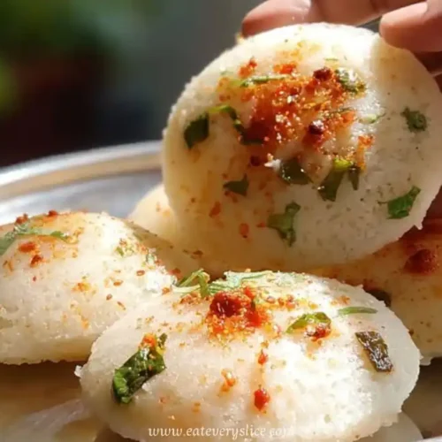Soft homemade idlis garnished with herbs and spices served on a steel plate