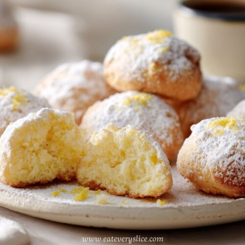 Soft Italian lemon cookies topped with powdered sugar and zest, arranged on plate with coffee in background