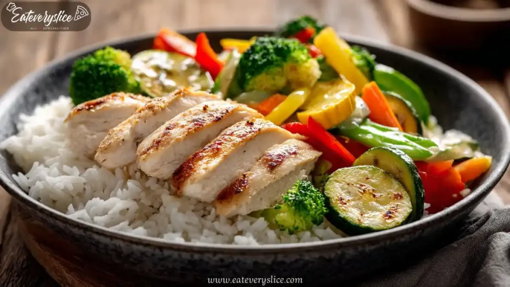grilled chicken and mixed vegetables served over white rice in a black bowl with colorful presentation