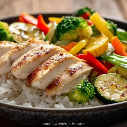 grilled chicken and mixed vegetables served over white rice in a black bowl with colorful presentation