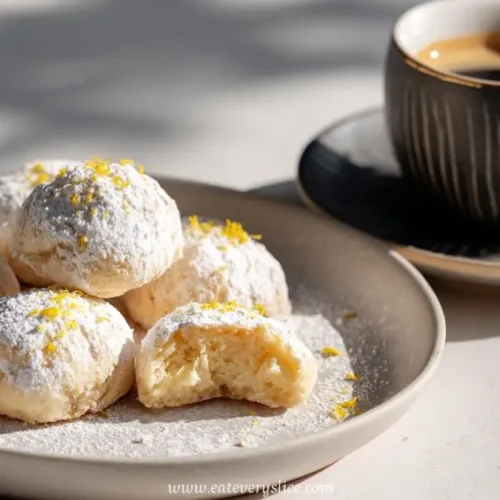 soft lemon cookies dusted with powdered sugar on a plate beside a cup of black coffee