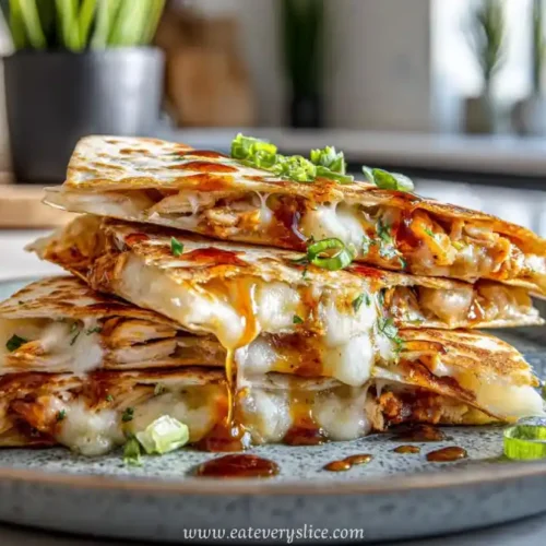 Stack of crispy chicken quesadilla slices with melted cheese and sweet sauce, garnished with scallions