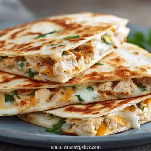 Stacked chicken quesadilla slices on a rustic plate with melted cheese and chopped herbs