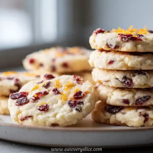 Stack of cranberry orange cookies with sugar crust and orange zest on ceramic plate