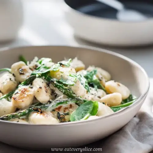 Creamy gnocchi with sautéed spinach and asparagus in a shallow beige bowl, served fresh