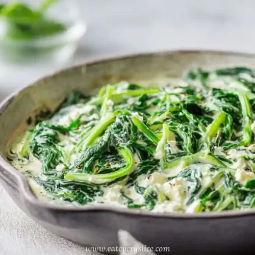 creamy spinach with feta cheese in rustic ceramic pan served hot on white table