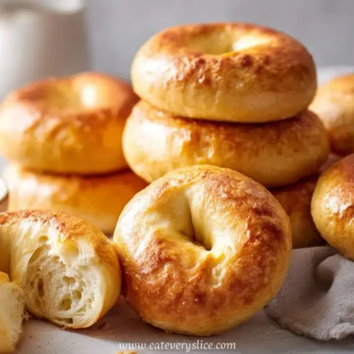 Stack of homemade golden yogurt bagels with one torn open in front and cream cheese on the side