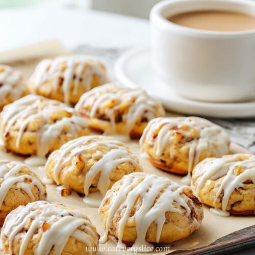 Glazed oven baked apple fritters on a tray with icing drizzle next to a cup of coffee